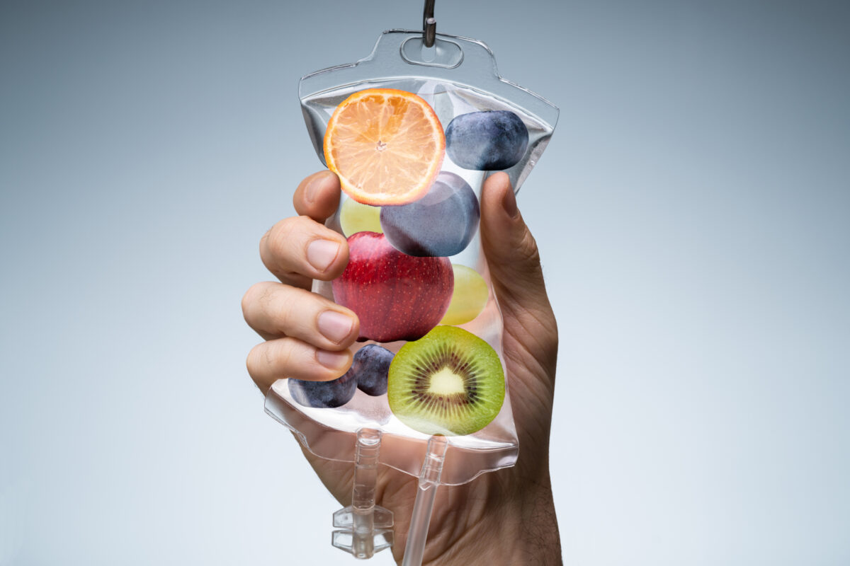 A hand squeezing an IV hydration bag filled with exotic and fresh fruit.