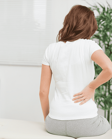 Back pain causing a woman to sit at the edge of her bed and hold her lower back.
