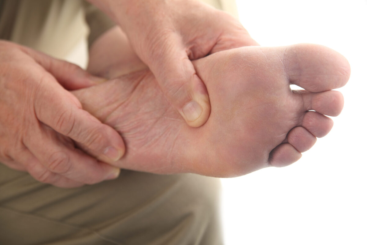 Close-up of a man massaging his bare foot to relieve diabetic foot pain.