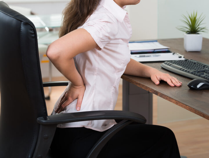 A businesswoman experiencing acute back and leg pain when sitting at her desk.