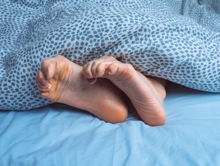 A close-up of painful legs at night causing a woman to curl her toes in bed and under a blanket.