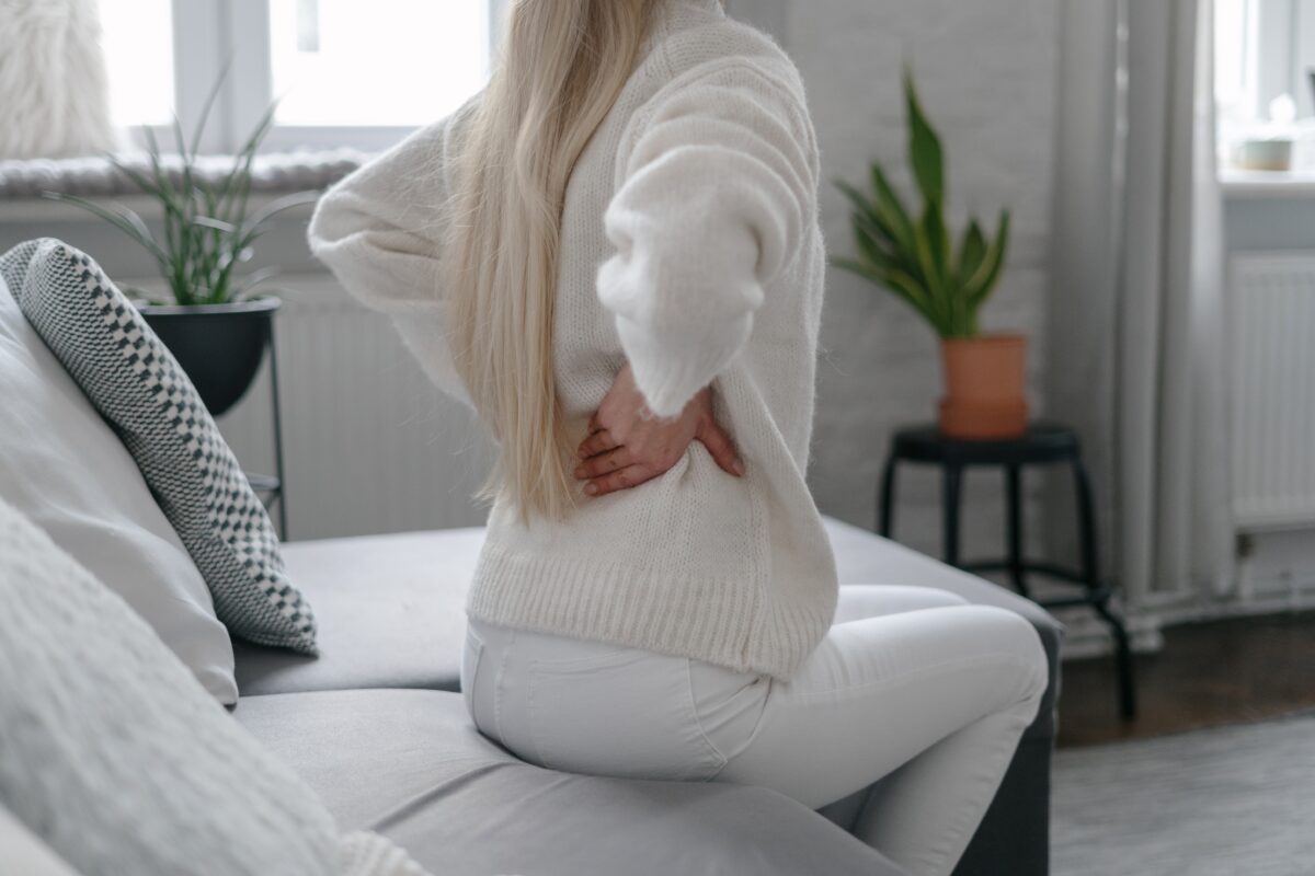 A lady holding her back and sitting on a couch, thinking about lower back pain treatment.