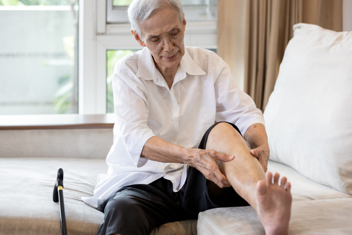 An older woman examines and rubs her leg on the couch at home as she suffers from nerve pain in leg issues.