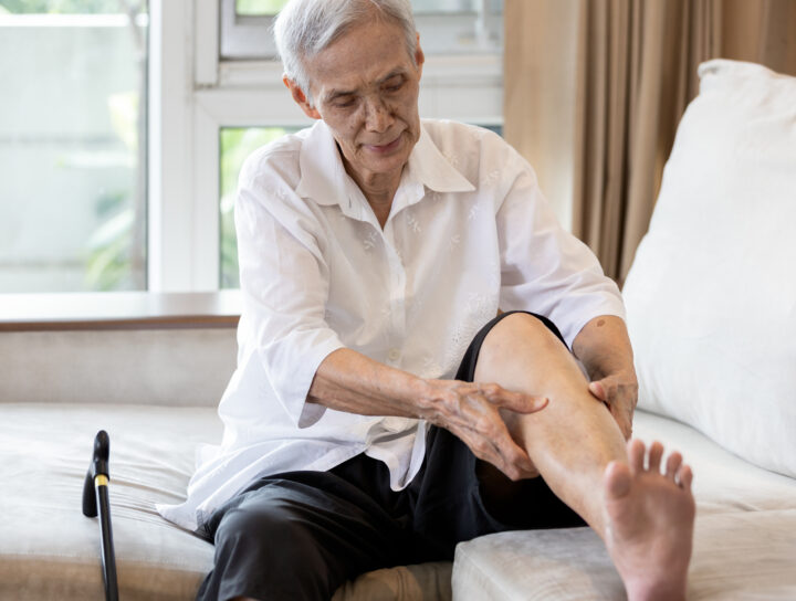 An older woman examines and rubs her leg on the couch at home as she suffers from nerve pain in leg issues.