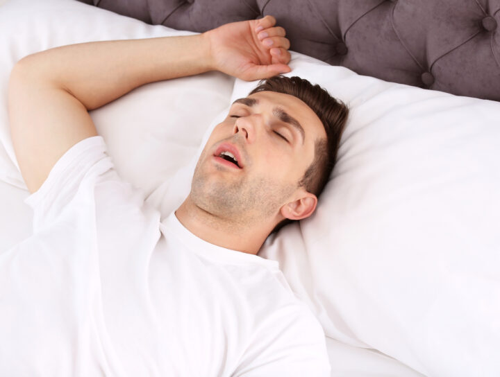 A man sleeping with his mouth open in bed, illustrating the need for sleep apnea treatment.