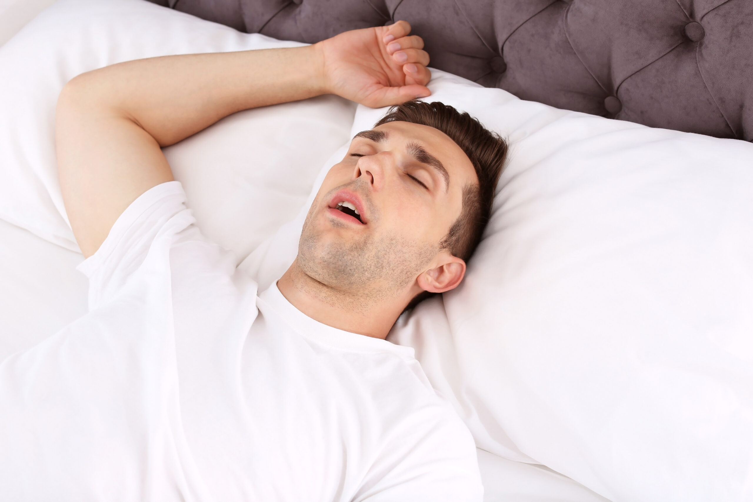 A man sleeping with his mouth open in bed, illustrating the need for sleep apnea treatment.