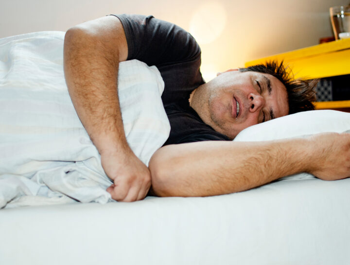 A large man sleeping with his mouth open in bed, and most likely soon considering treatment for sleep apnea.