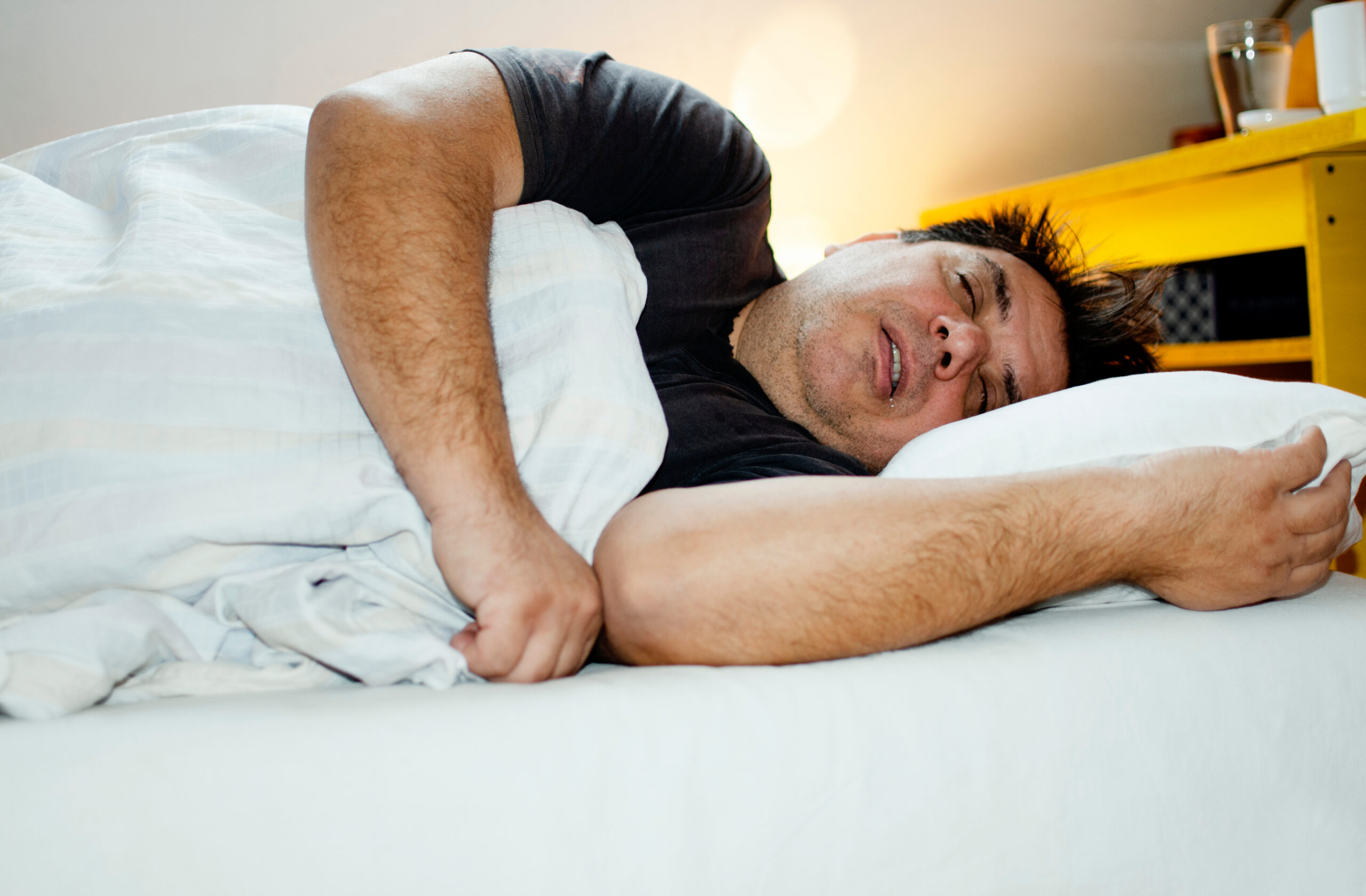 A large man sleeping with his mouth open in bed, and most likely soon considering treatment for sleep apnea.