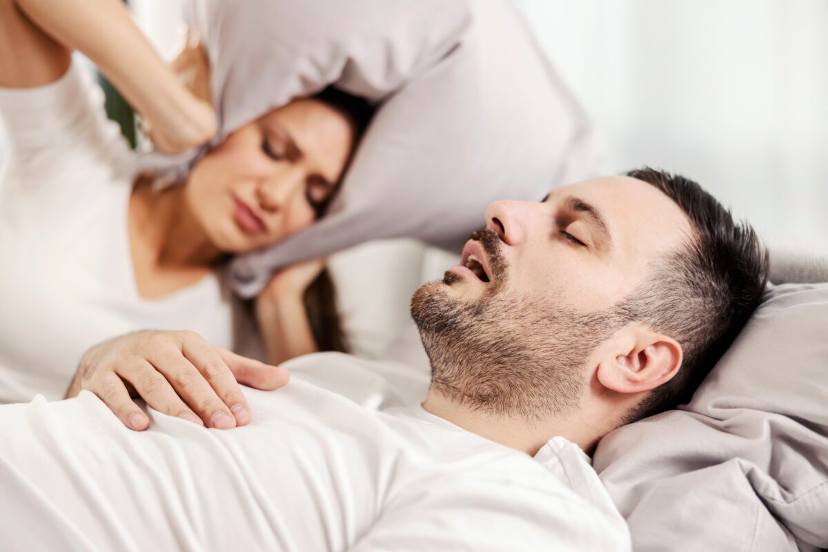 Getting sleep apnea help can slip past many people, including this image of a husband snoring while his wife has a hard time sleeping next to him.