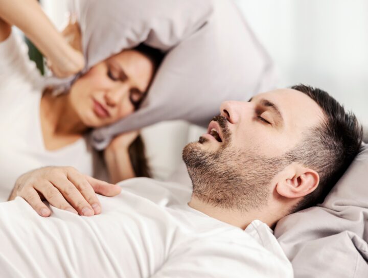 Getting sleep apnea help can slip past many people, including this image of a husband snoring while his wife has a hard time sleeping next to him.