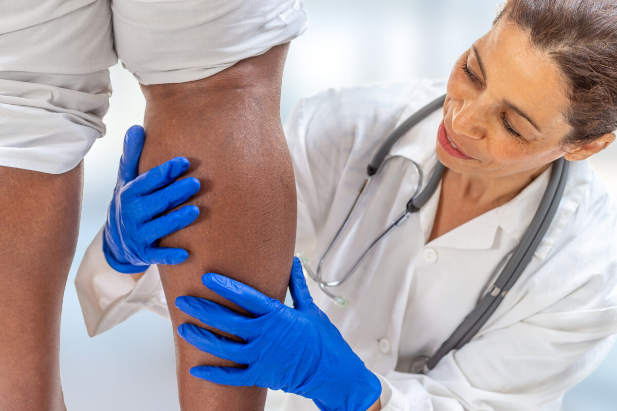 A doctor providing varicose veins treatment to an older lady who is a patient as her leg is inspected.