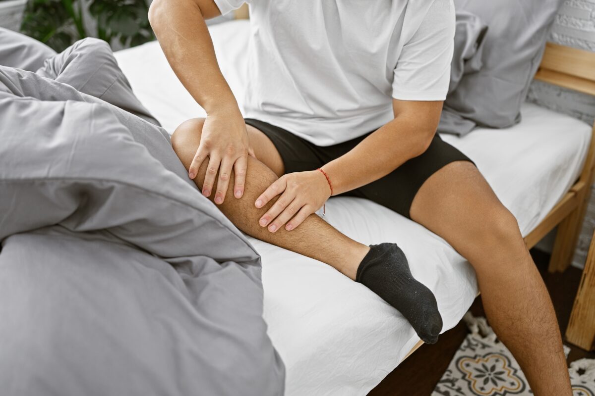 A middle-age man, having just woken up from a tiring night's rest, deals with restless legs as he sits on the side of his bed.