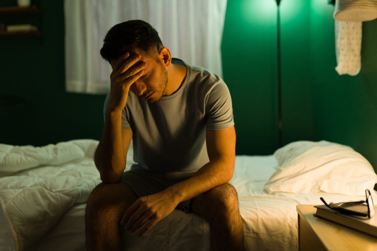A sleepless man on the edge of his bed with the light on late at night, considering dental sleep device treatment.
