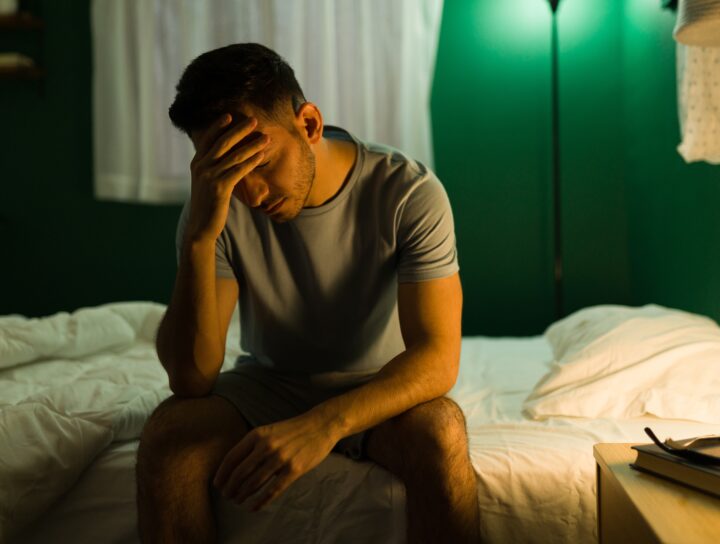 A sleepless man on the edge of his bed with the light on late at night, considering dental sleep device treatment.