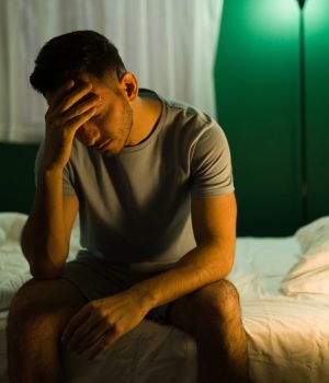 A sleepless man on the edge of his bed with the light on late at night, considering dental sleep device treatment.