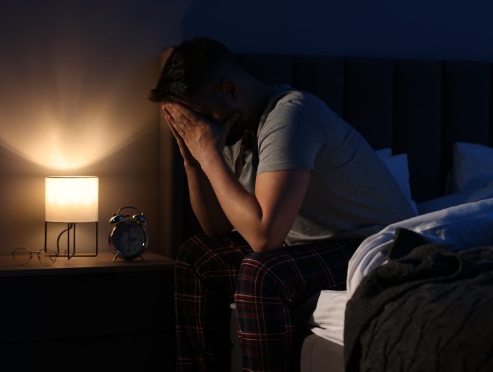 A sleepless man on the edge of his bed, considering CPAP alternatives.