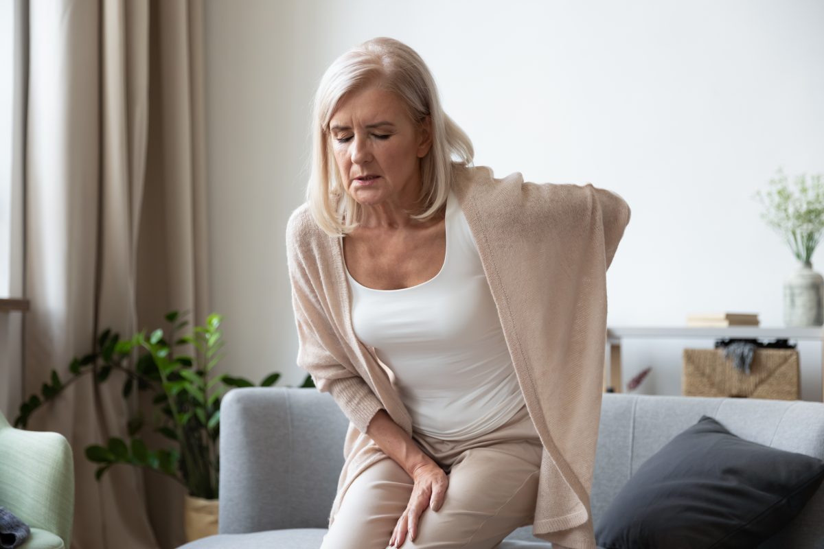 The best sciatic nerve pain relief options are available to try, as illustrated by this elderly senior woman standing up in pain from her living room couch.