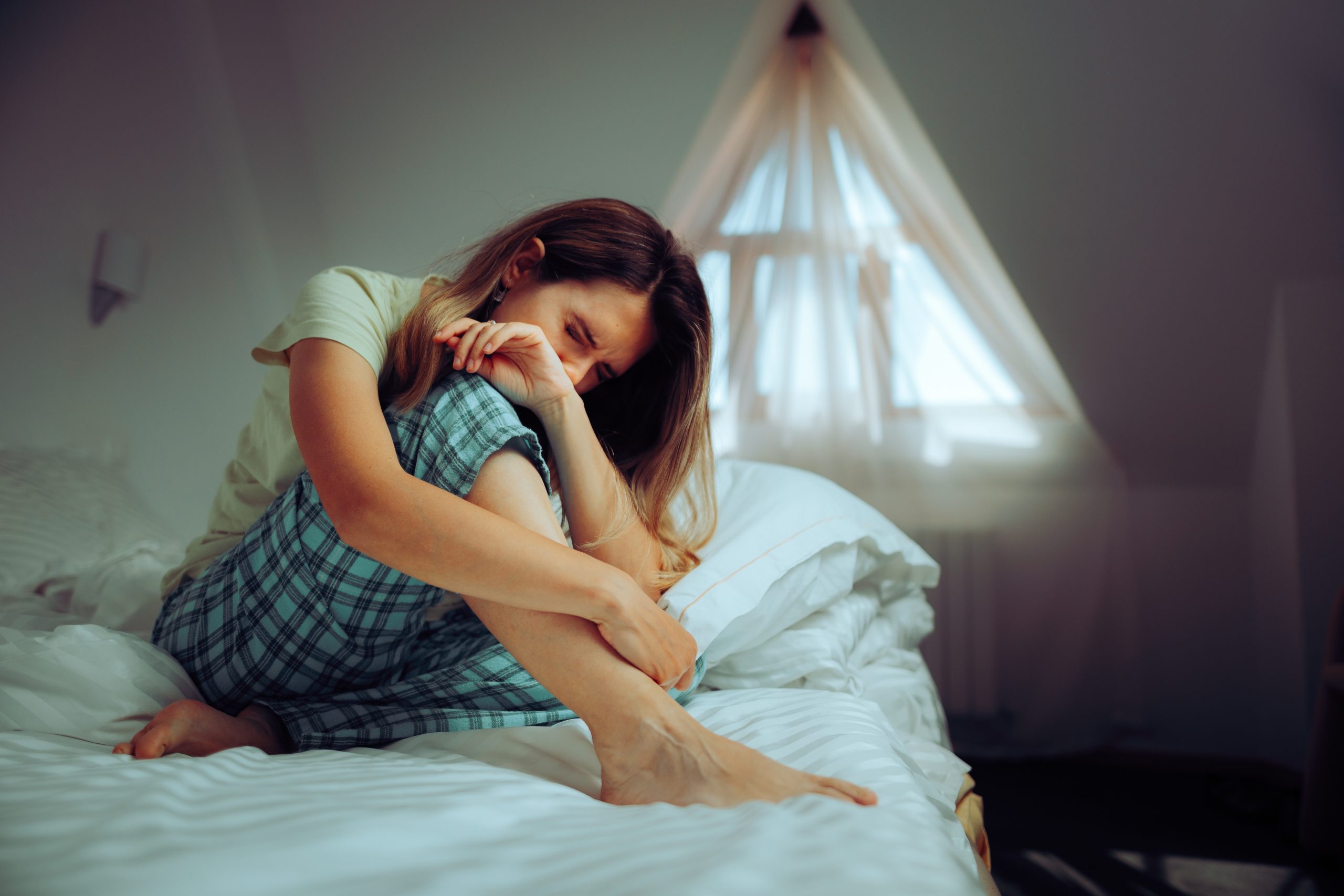 A young lady experiencing calf cramps at night, suffering from pain on the edge of her bed.