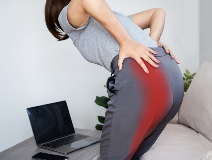This middle-age woman who works from home on her couch with a lap top is also in need of hip and leg pain treatment, as evidenced by the discomfort she feels as she holds her hips.