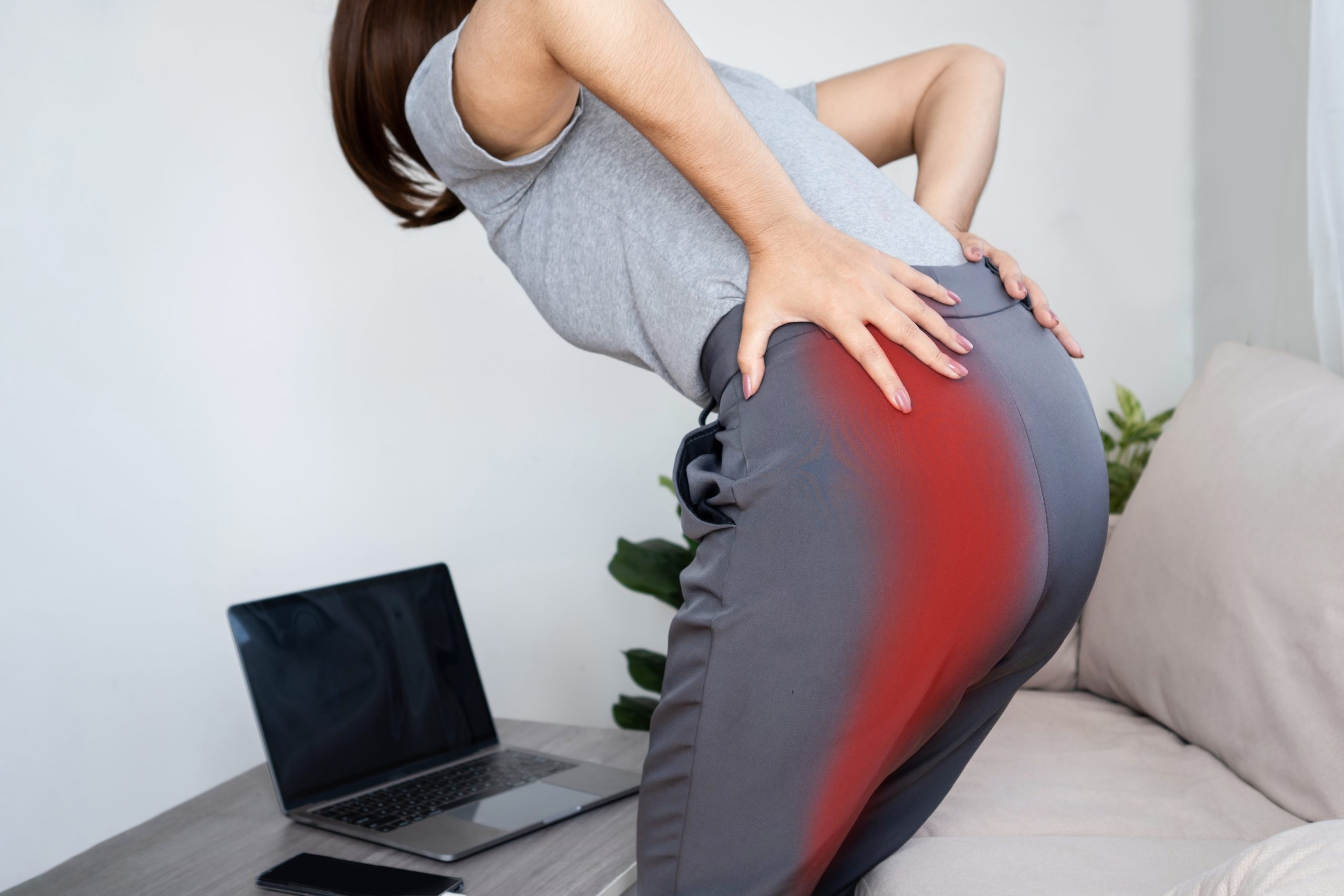 This middle-age woman who works from home on her couch with a lap top is also in need of hip and leg pain treatment, as evidenced by the discomfort she feels as she holds her hips.