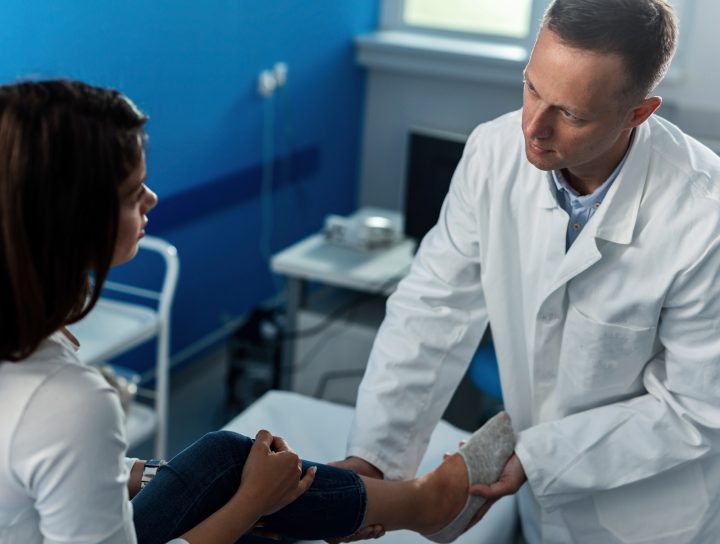A leg cramp doctor being consulted by a middle-aged woman as he holds her calf and foot for inspection.