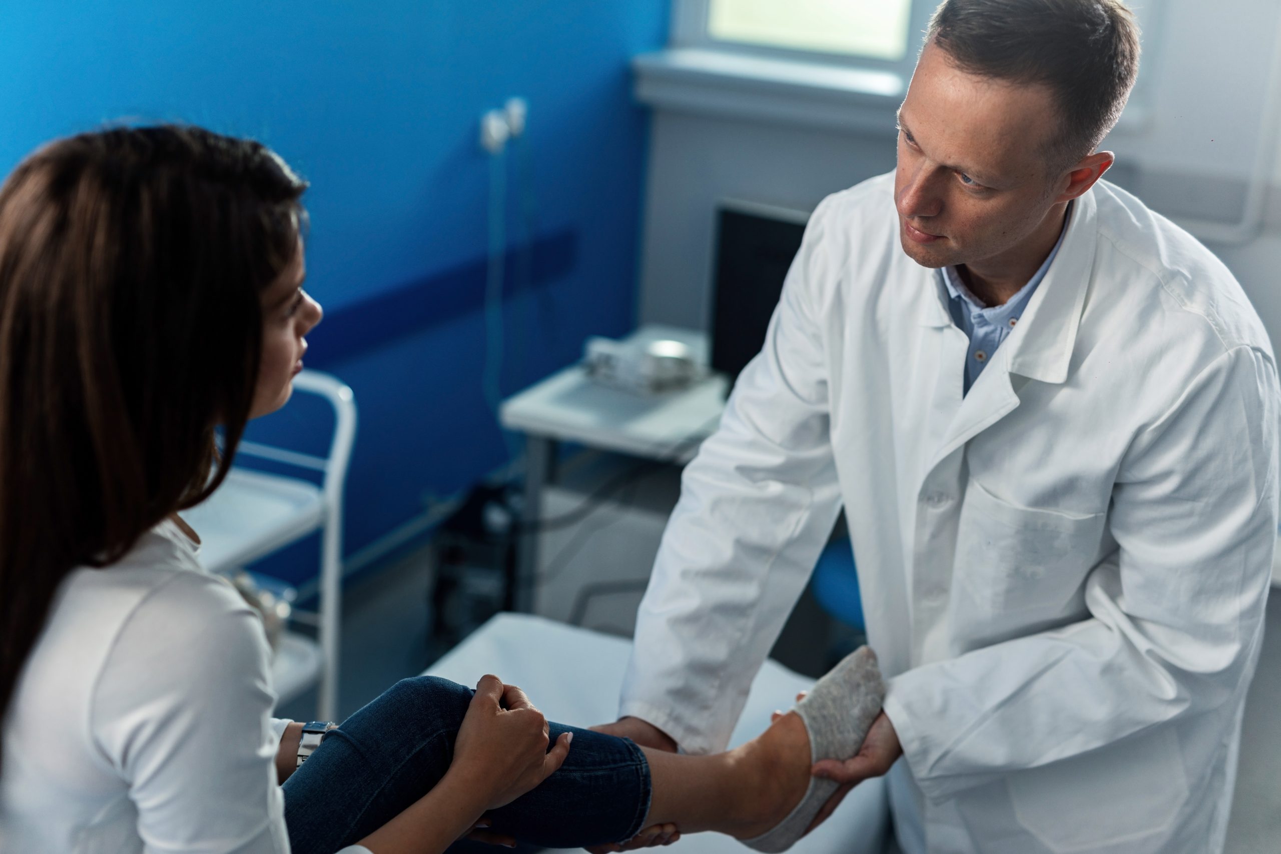A leg cramp doctor being consulted by a middle-aged woman as he holds her calf and foot for inspection.