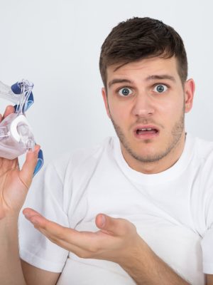 Close-up,Of,Shocked,Young,Man,Holding,Cpap,Machine,Mask