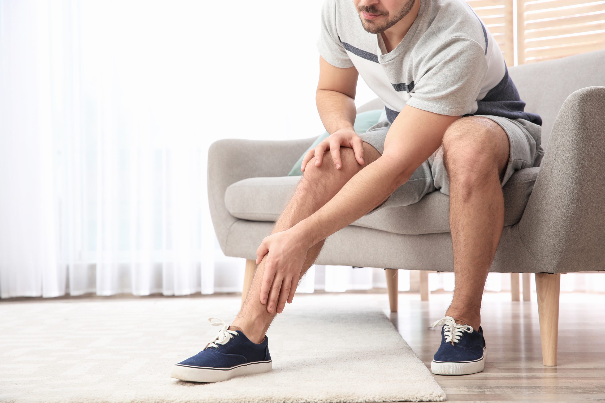 A man sitting on his couch, dealing with painful lower legs and massaging one of them.