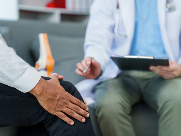 A pain management doctor examining a patient who is holding his knee.
