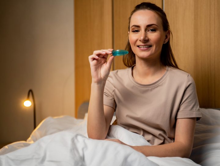 An attractive woman uses a custom sleep mouth device at night in bed.