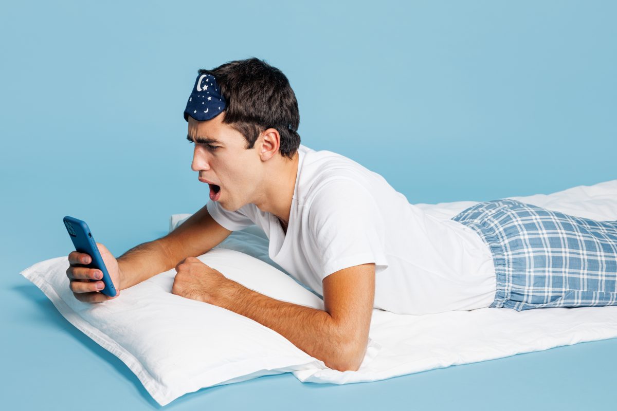A man laying down, reading an article on his phone regarding MAD sleep apnea devices.