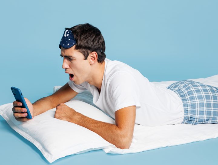 A man laying down, reading an article on his phone regarding MAD sleep apnea devices.