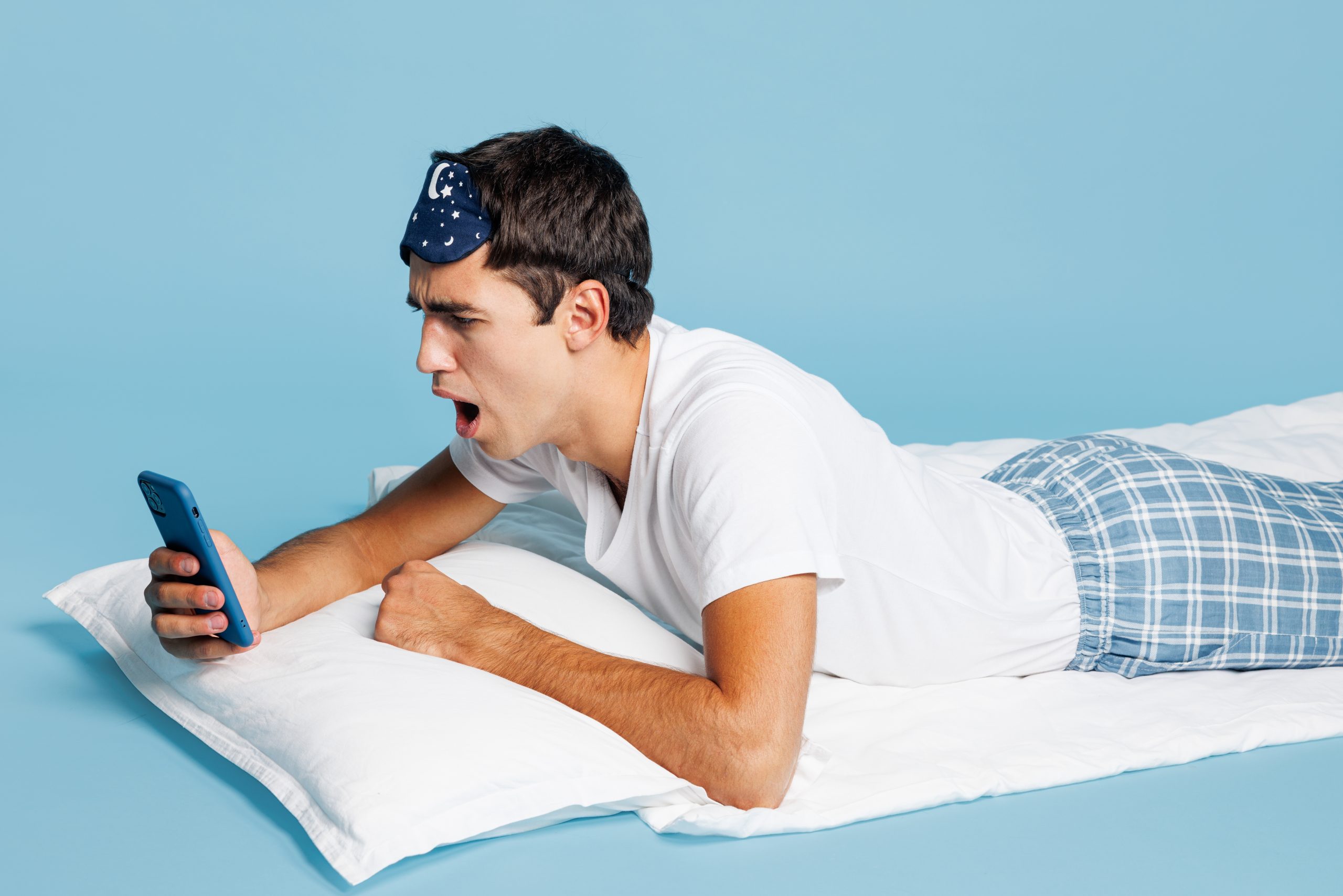 A man laying down, reading an article on his phone regarding MAD sleep apnea devices.