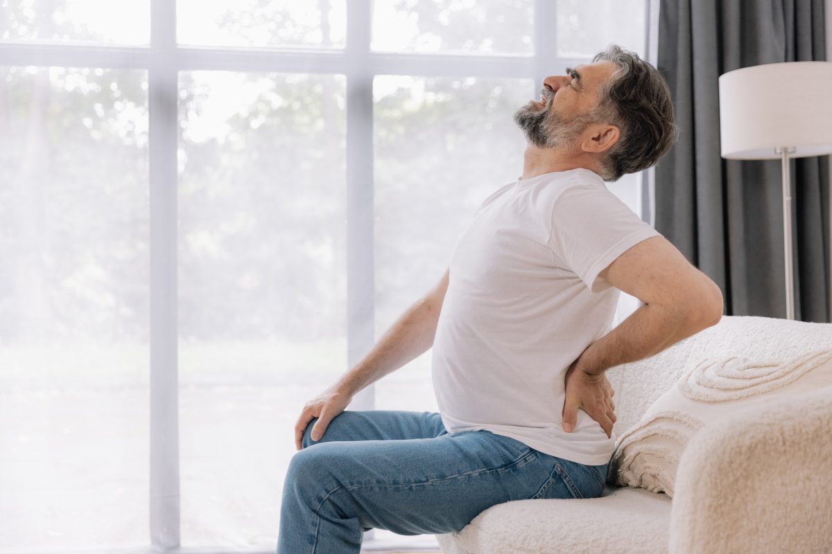 A middle-aged man deals with sciatica and lower leg pain, holding his back while sitting on a couch.