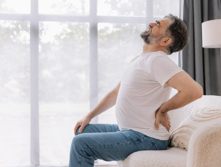 A middle-aged man deals with sciatica and lower leg pain, holding his back while sitting on a couch.