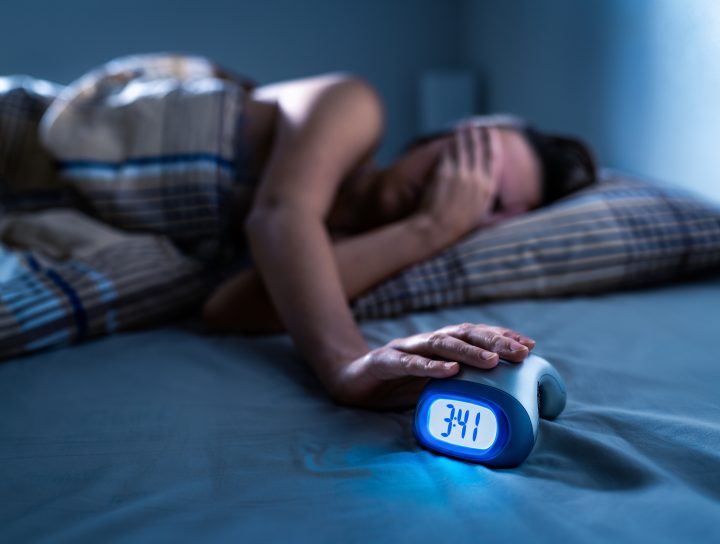 A lady in the middle of the night covering her eyes while laying in bed, considering sleep apnea oral devices as her rest is disrupted.