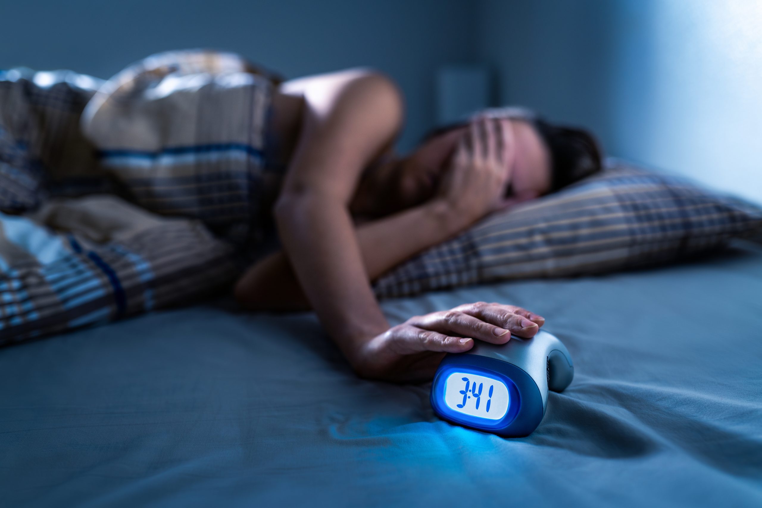 A lady in the middle of the night covering her eyes while laying in bed, considering sleep apnea oral devices as her rest is disrupted.