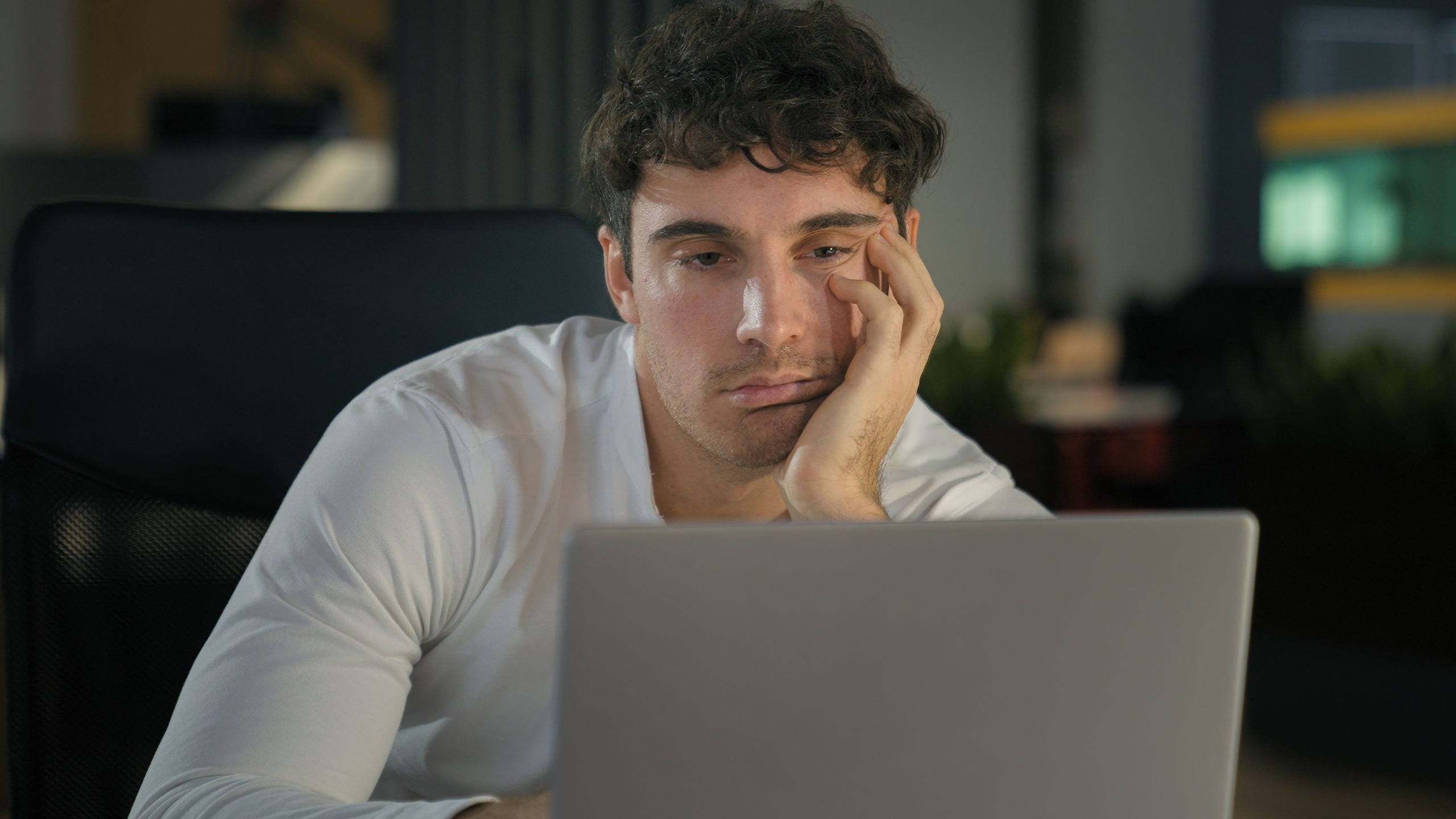 A tired man sitting in front of his lap top and working, considering the benefits of a home sleep test.