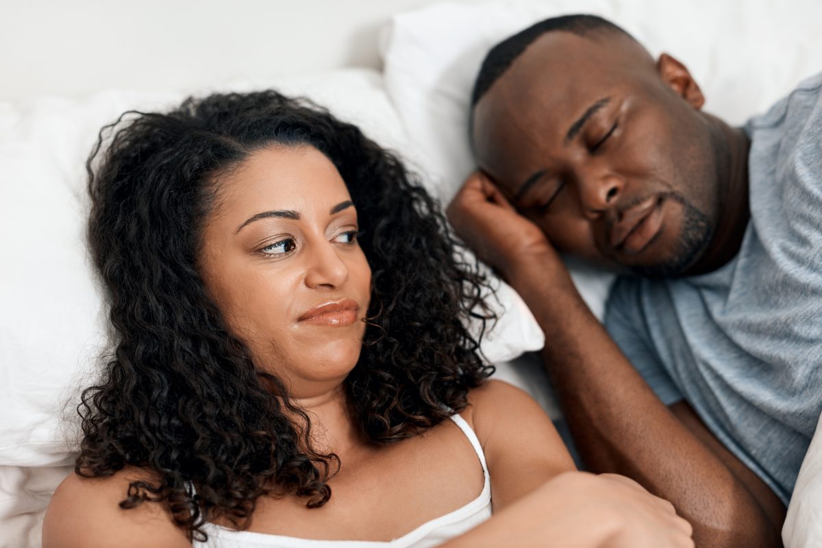 A wife looking at her husband in bed who is dealing with sleep apnea, considering treatment for sleep apnea.