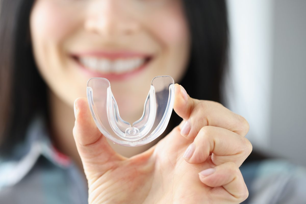 A smiling woman illustrating the concept of the HST testing process by holding up a sleep apnea mouthguard.
