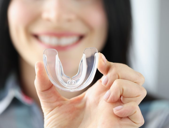 A smiling woman illustrating the concept of the HST testing process by holding up a sleep apnea mouthguard.