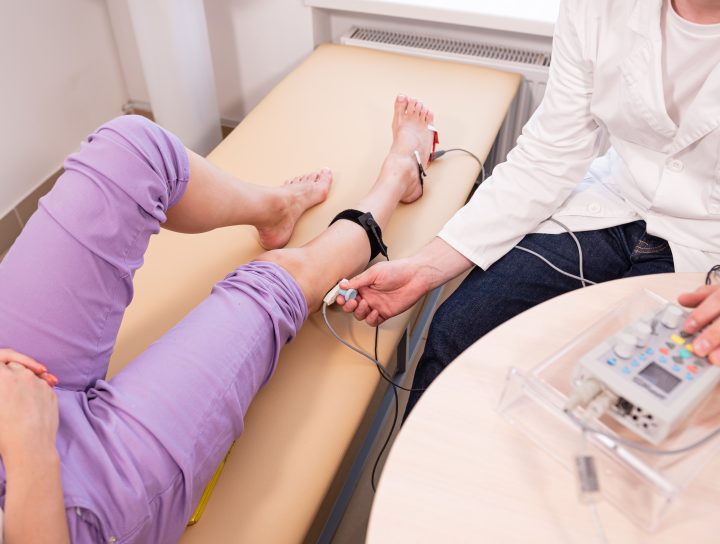 A patient dealing with leg cramps at night lies on a clinic bed as a pain management specialist performs an EMG on the patient's legs.