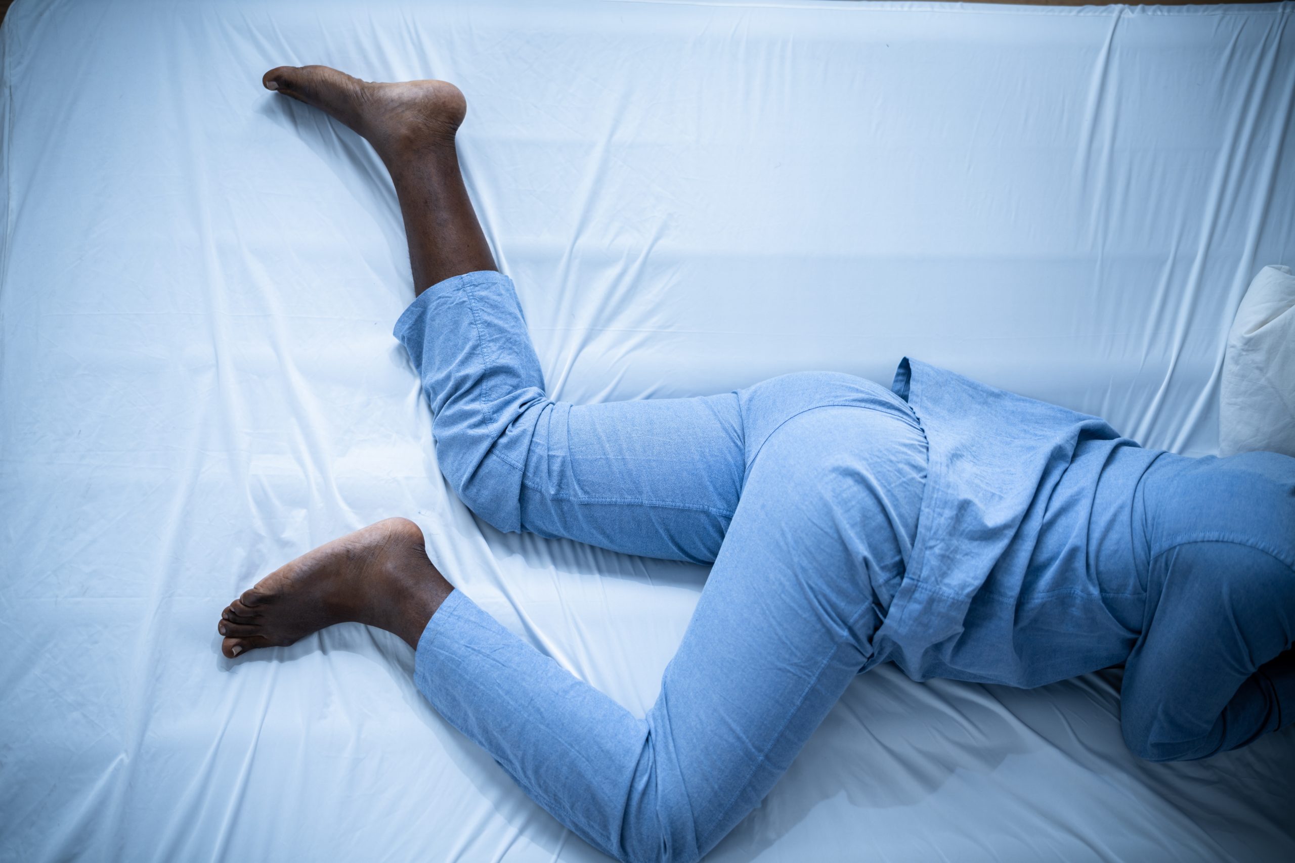 A body in a bed at night, with the individual struggling through restless leg syndrome.